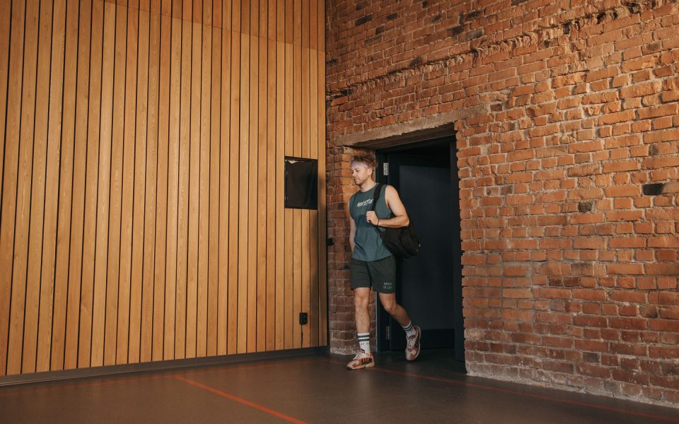 A member with a gym bag walks into a gym hall through a side door.